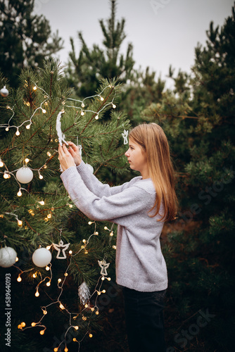 beautiful girl in winter pine forest. decorates the Christmas tree with bright lights and toys in the forest. Christmas presents in the forest under the tree. Christmas tree lights. New Year's decor 