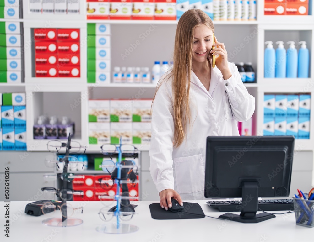 Young caucasian woman pharmacist talking on smartphone using computer at pharmacy Young caucasian woman pharmacist talking on smartphone using computer at pharmacy