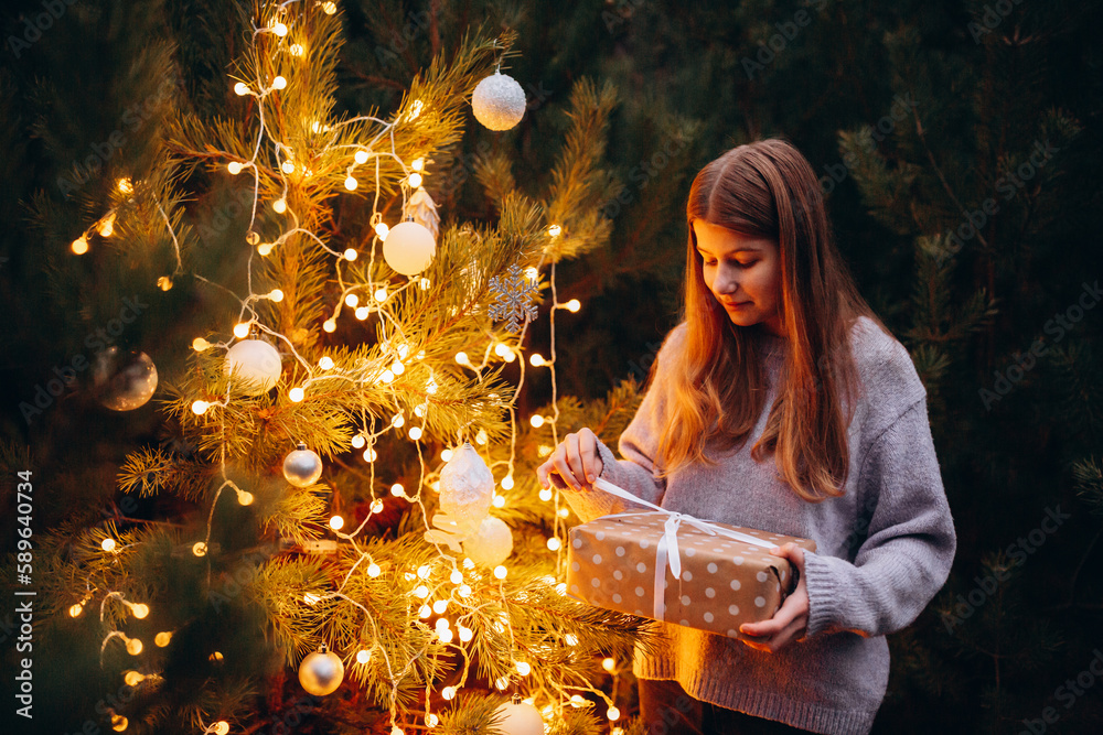 beautiful girl in winter pine forest. decorates the Christmas tree with bright lights and toys in the forest. Christmas presents in the forest under the tree. Christmas tree lights. New Year's decor beautiful girl in winter pine forest. decorates the Christmas tree with bright lights and toys in the forest. Christmas presents in the forest under the tree. Christmas tree lights. New Year's decor