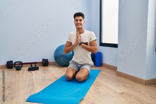 Young hispanic man smiling confident training yoga at sport center
