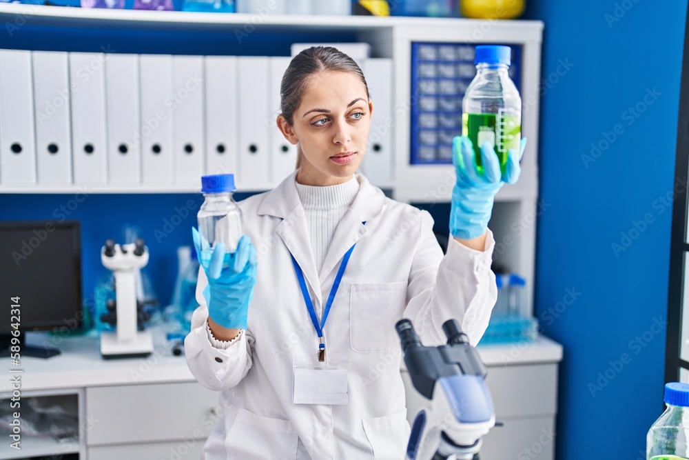 Young woman scientist holding bottles with liquid at laboratory