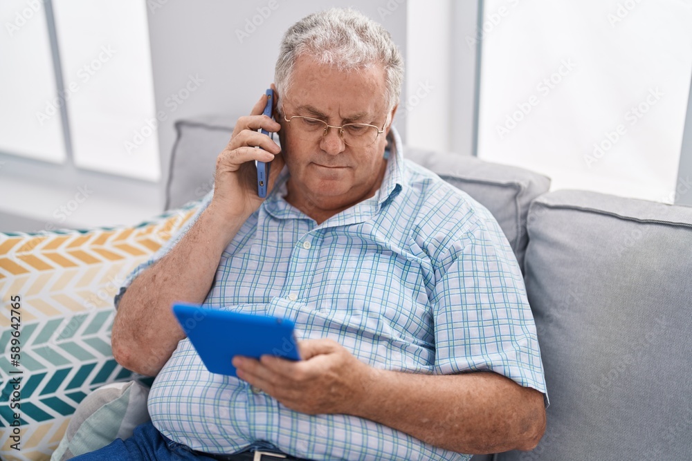 Middle age grey-haired man talking on smartphone using touchpad at home Middle age grey-haired man talking on smartphone using touchpad at home