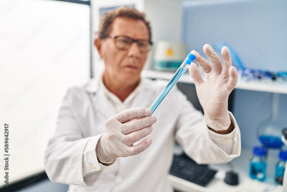 Middle age man wearing scientist uniform looking test tube at laboratory Middle age man wearing scientist uniform looking test tube at laboratory