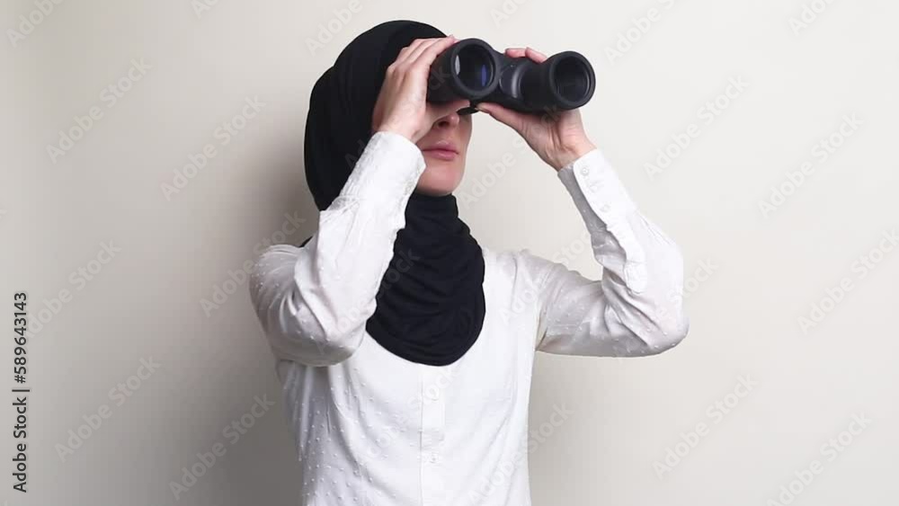 Young woman in hijab looking through binoculars on white background. Young woman in hijab looking through binoculars on white background.
