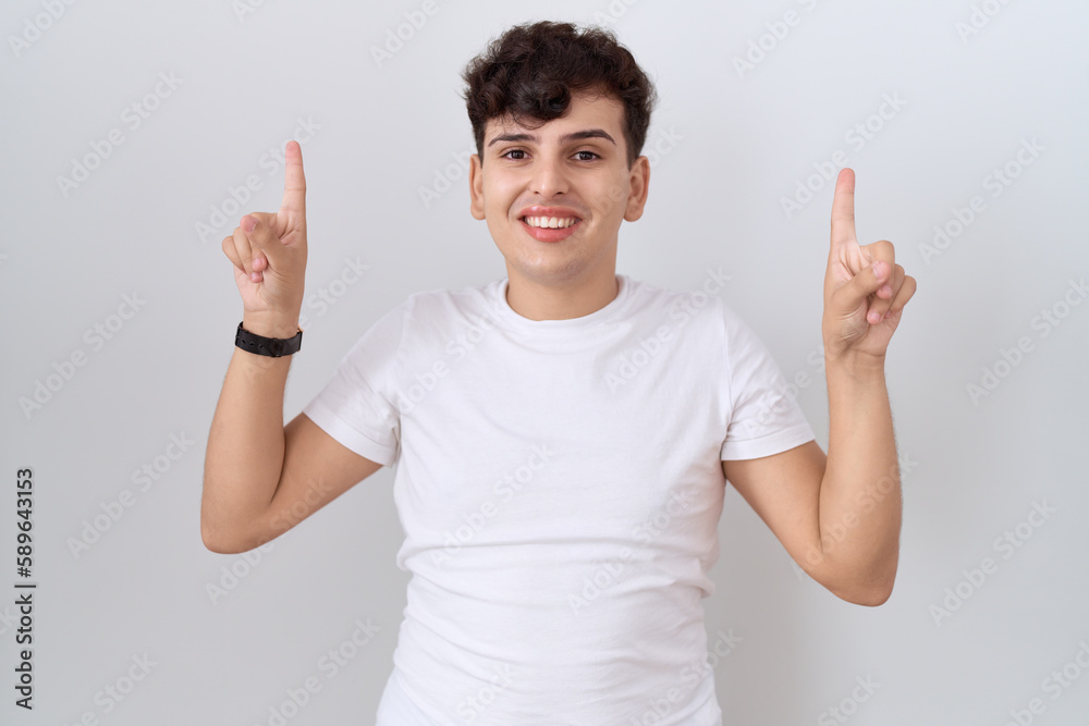 Young non binary man wearing casual white t shirt smiling amazed and surprised and pointing up with fingers and raised arms. Young non binary man wearing casual white t shirt smiling amazed and surprised and pointing up with fingers and raised arms.