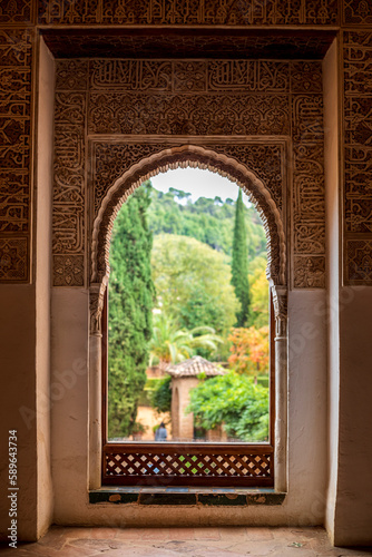 Window decorated with reliefs from the Nasrid palaces of the Alhambra in Granada, Spain with the blurred and colorful gardens in the background