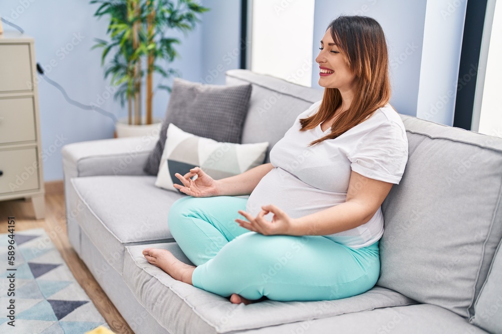 Young pregnant woman doing yoga exercise sitting on sofa at home Young pregnant woman doing yoga exercise sitting on sofa at home