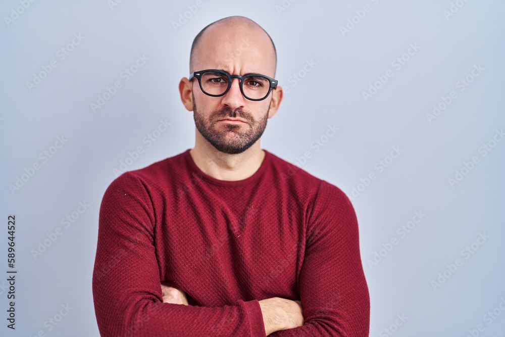 Young bald man with beard standing over white background wearing glasses skeptic and nervous, disapproving expression on face with crossed arms. negative person. Young bald man with beard standing over white background wearing glasses skeptic and nervous, disapproving expression on face with crossed arms. negative person.