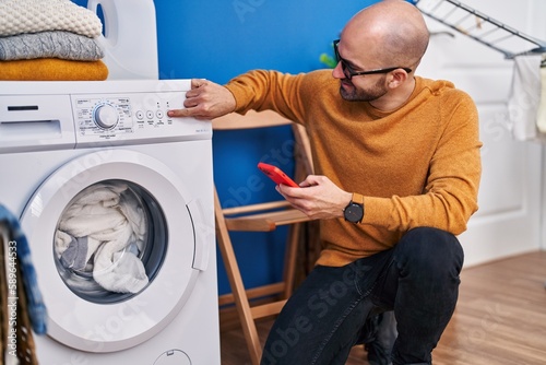 Young man using smartphone turning on washing machine at laundry room