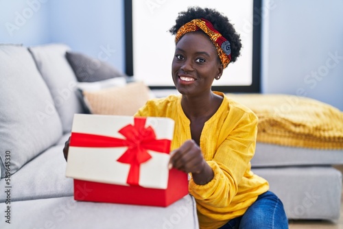 Young african american woman unboxing present package sitting on floor at home