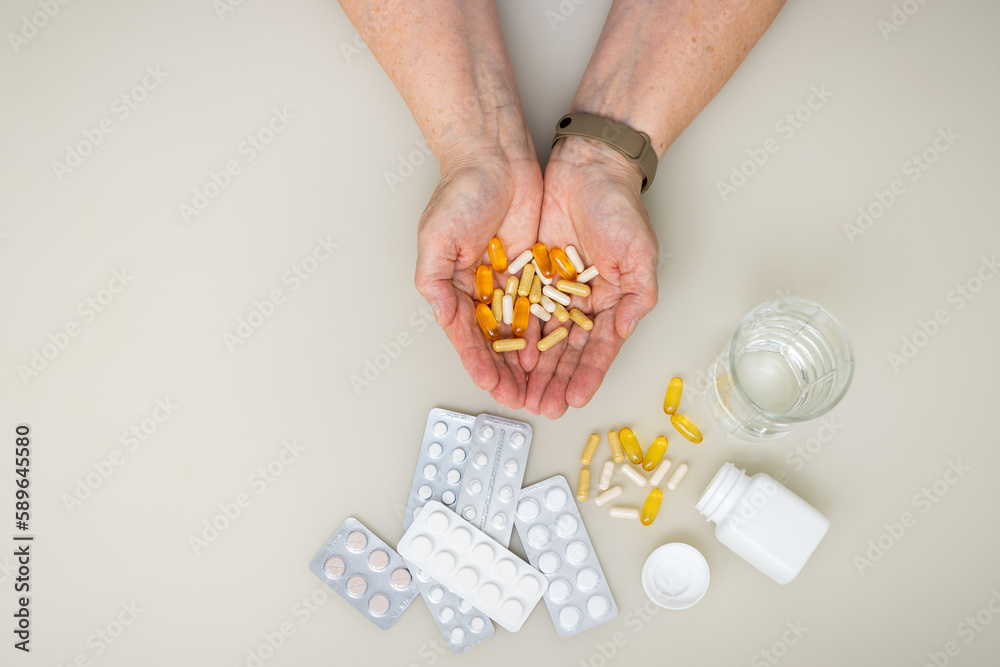 Obraz premium Senior woman with wrinkled old hands at the table holding different capsules and vitamins, full palms with pills for treatment. Healthcare and medicine concept, top view