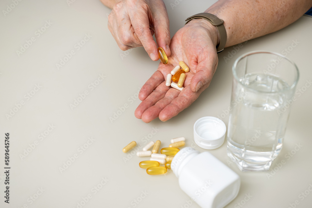 Senior woman with wrinkled old hands at the table holding Omega 3 capsule, vitamins and various pills for treatment. Healthcare and medicine concept Senior woman with wrinkled old hands at the table holding Omega 3 capsule, vitamins and various pills for treatment. Healthcare and medicine concept