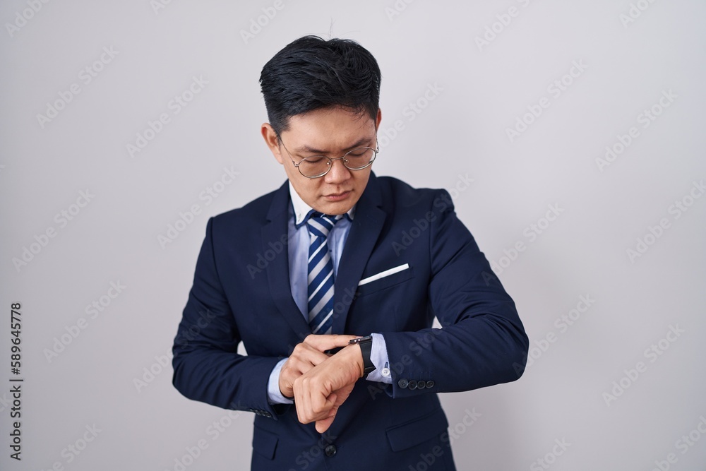 Young asian man wearing business suit and tie checking the time on wrist watch, relaxed and confident Young asian man wearing business suit and tie checking the time on wrist watch, relaxed and confident