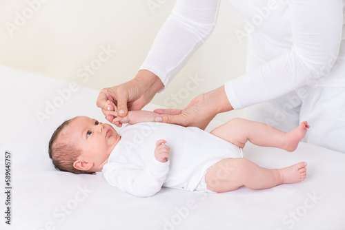 Loving Mother or Physiotherapist Doing Finger Exercises To Newborn Baby Girl On Bed At Home