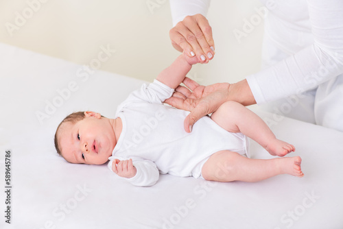 Loving Mother or Physiotherapist Doing Palm Exercises To Newborn Baby Girl On Bed At Home