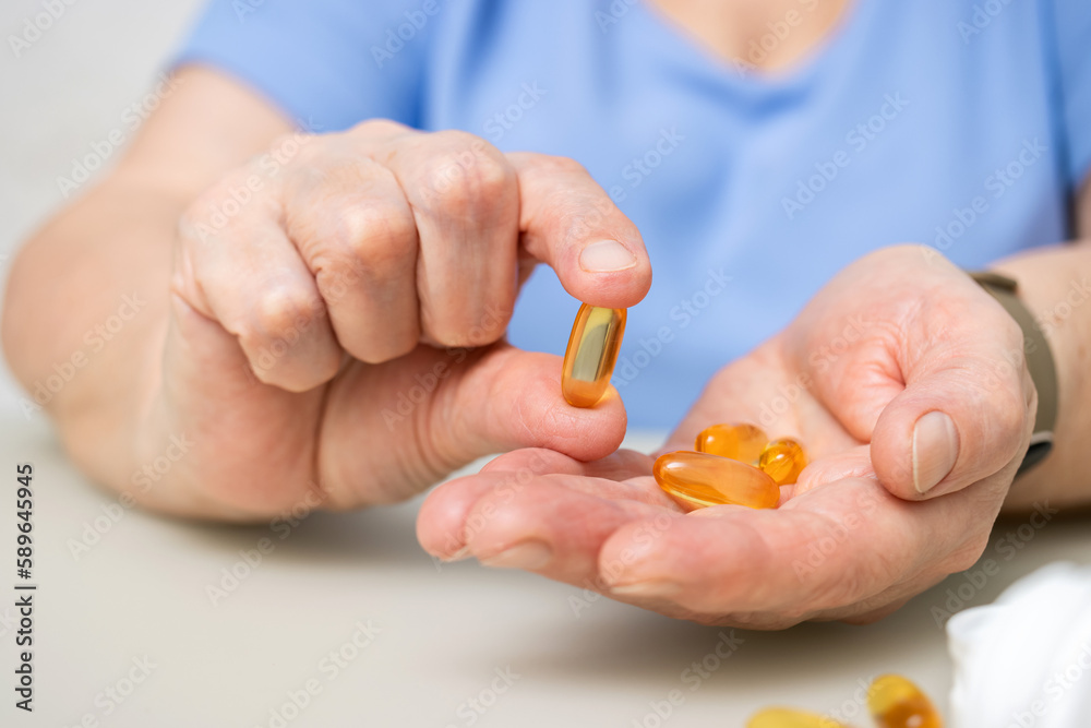 Senior woman with wrinkled old hands at the table holding omega 3 yellow capsules, fish oil pills, Healthcare and medicine concept