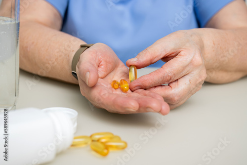 Senior woman with wrinkled old hands at the table holding omega 3 yellow capsules, fish oil pills, Healthcare and medicine concept