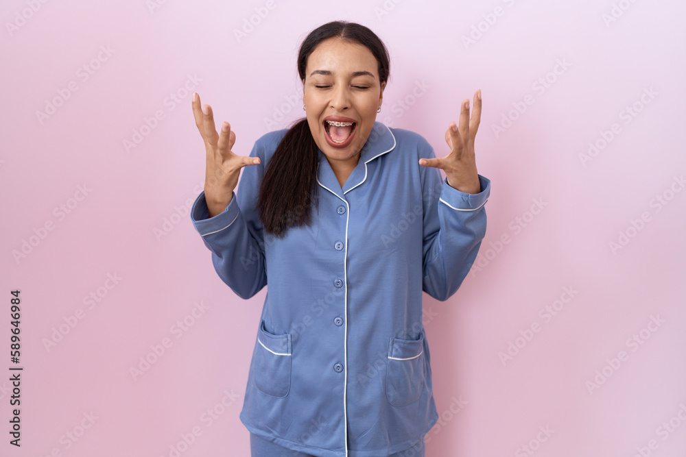 Young arab woman wearing blue pajama celebrating mad and crazy for success with arms raised and closed eyes screaming excited. winner concept