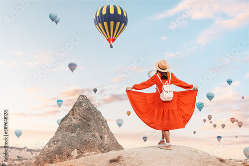 girl watching the hot air balloons take flight in the scenic landscape of Cappadocia. She dressed in a delicate summer dress and hat