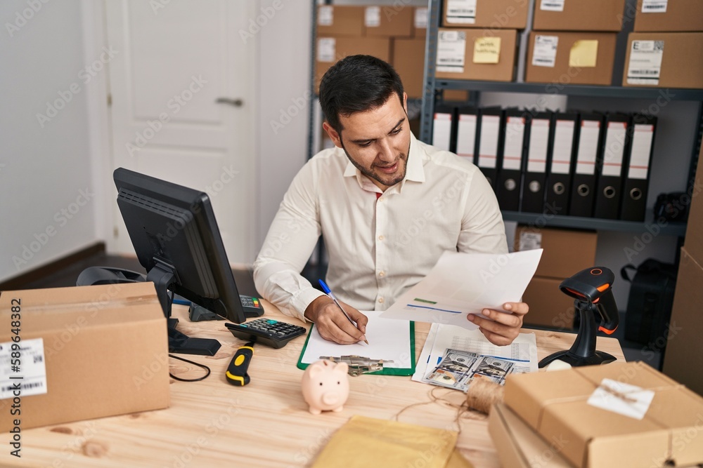 Young hispanic man e-commerce business worker writing on document at office Young hispanic man e-commerce business worker writing on document at office
