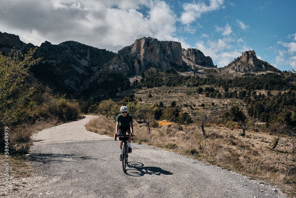 Woman cyclist riding a gravel bike with a view of the spanish mountains.Fit athlete wearing sportswear and helmet. Sports motivation image.