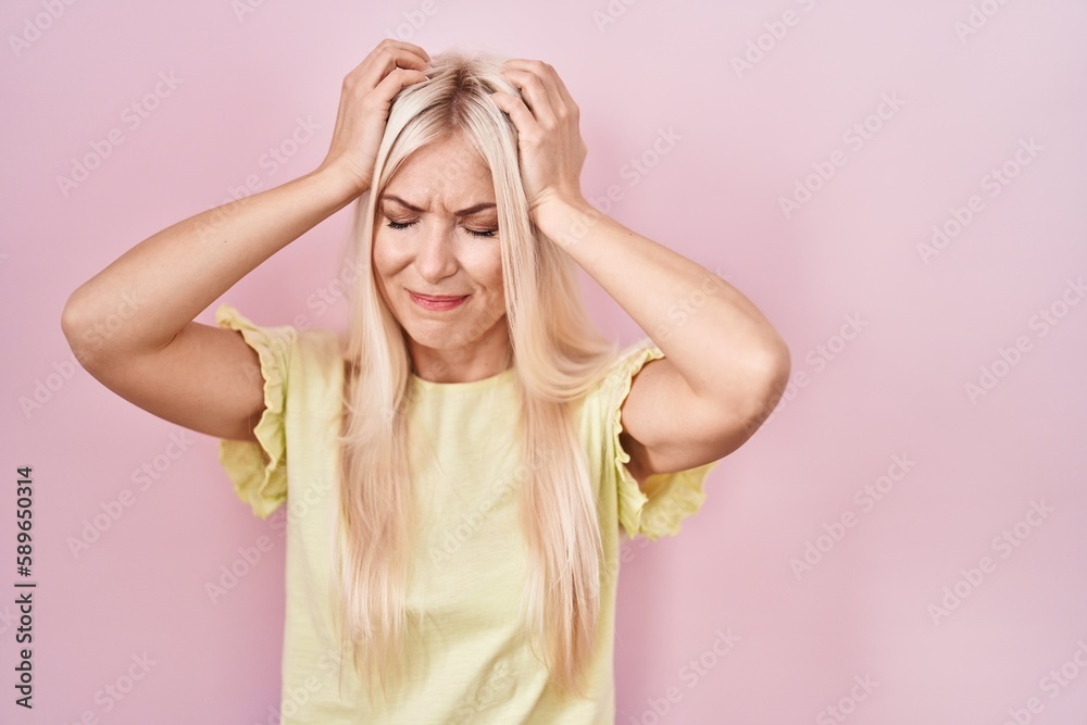 Caucasian woman standing over pink background suffering from headache desperate and stressed because pain and migraine. hands on head. Caucasian woman standing over pink background suffering from headache desperate and stressed because pain and migraine. hands on head.
