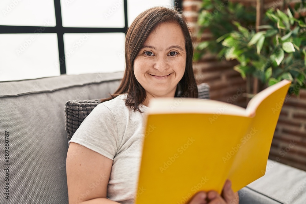 Down syndrome woman reading book sitting on sofa at home Down syndrome woman reading book sitting on sofa at home