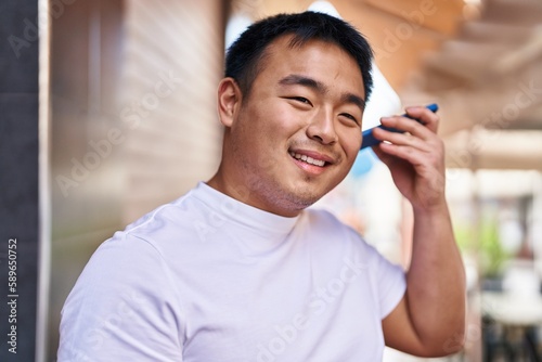 Young chinese man smiling confident listening audio message by the smartphone at street