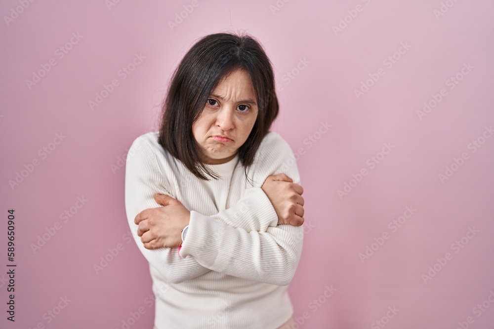 Woman with down syndrome standing over pink background shaking and freezing for winter cold with sad and shock expression on face Woman with down syndrome standing over pink background shaking and freezing for winter cold with sad and shock expression on face