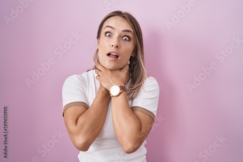 Blonde caucasian woman standing over pink background shouting suffocate because painful strangle. health problem. asphyxiate and suicide concept.
