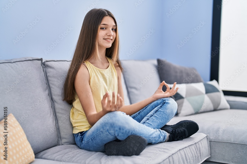 Adorable girl doing yoga exercise sitting on sofa at home Adorable girl doing yoga exercise sitting on sofa at home