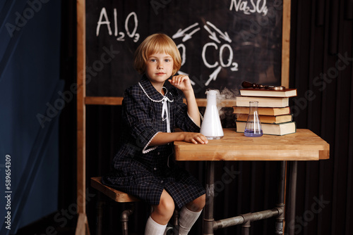 One little Caucasian girl Schoolgirl is sitting at the table conducting a chemical experiment in a flask of chemical equipment. The concept of learning and education, front view.