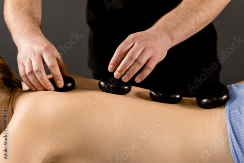 Masseur placed hot stone on the back of woman. Manual therapy in spa.