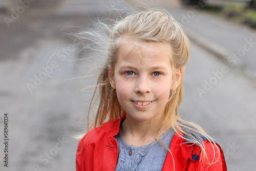 Blond preteen girl wearing red coat smiling and looking straight. Outdoor portrait