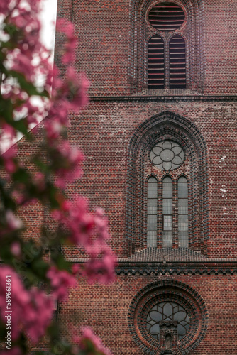 Flowering shrub with pink flowers in the foreground and a red brick church with stained glass windows