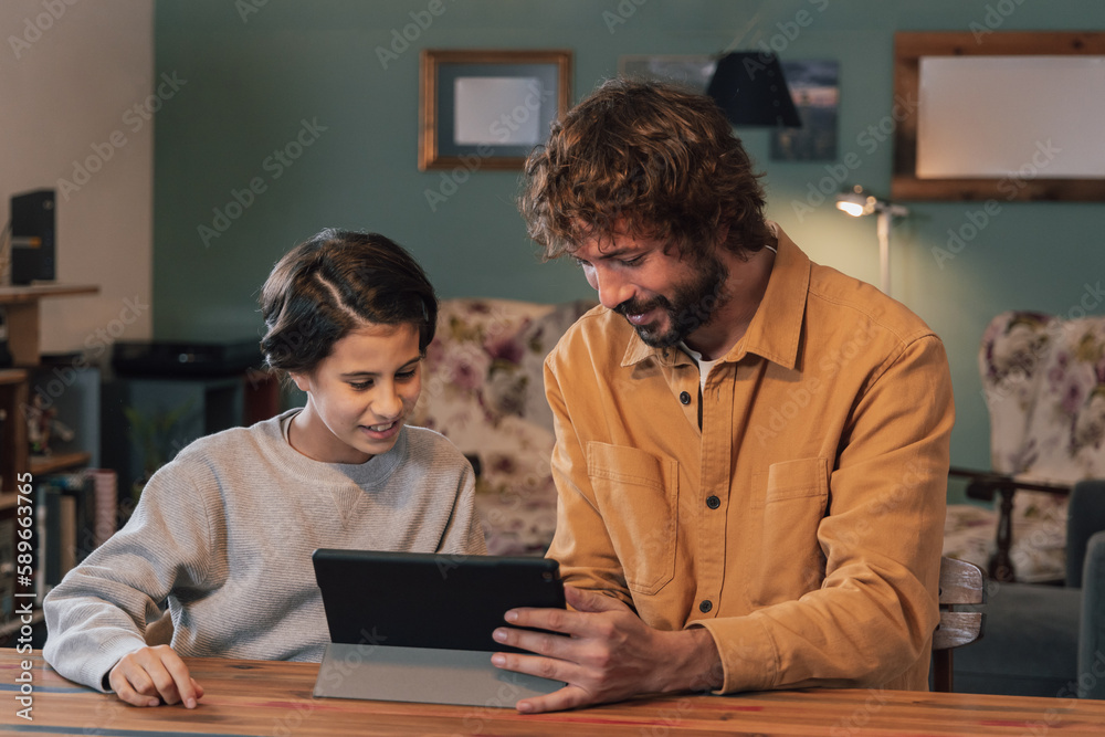Young bearded man showing something on the tablet to a teenage girl at the dinner table at home Young bearded man showing something on the tablet to a teenage girl at the dinner table at home