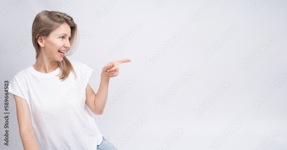 Blonde woman profile with long hair looking side pointing finger with calm relaxed smile. Long horizontal background. White clothe t-shirt and solid gray background Blonde woman profile with long hair looking side pointing finger with calm relaxed smile. Long horizontal background. White clothe t-shirt and solid gray background