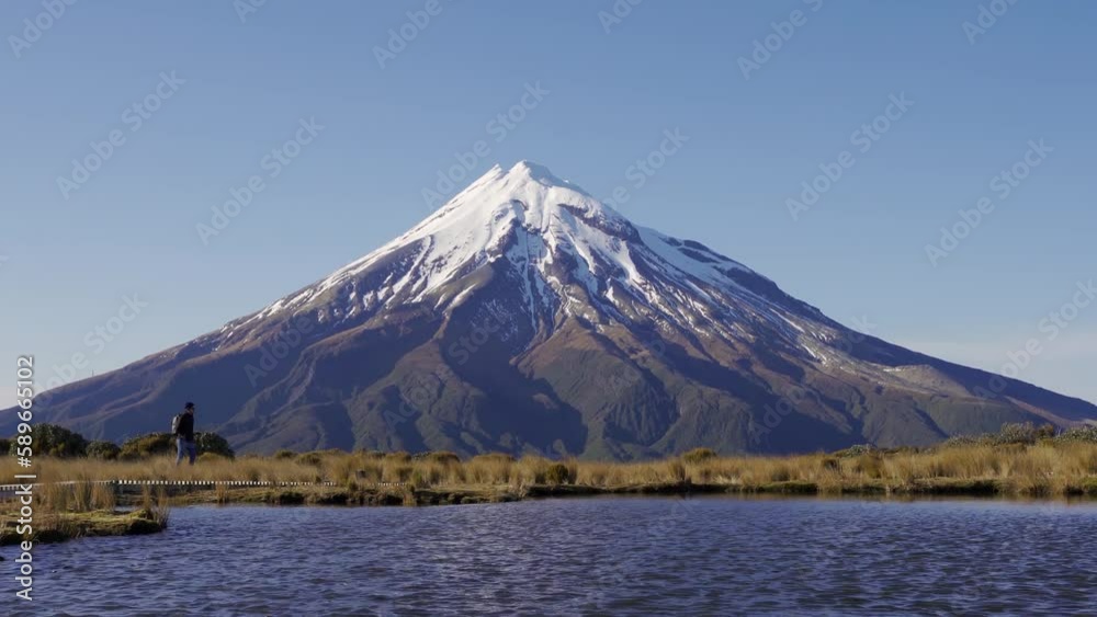 Backpacker walking by Pouakai Reflective Tarn with the majestic Mount Taranic behind. New Zealand. Backpacker walking by Pouakai Reflective Tarn with the majestic Mount Taranic behind. New Zealand.