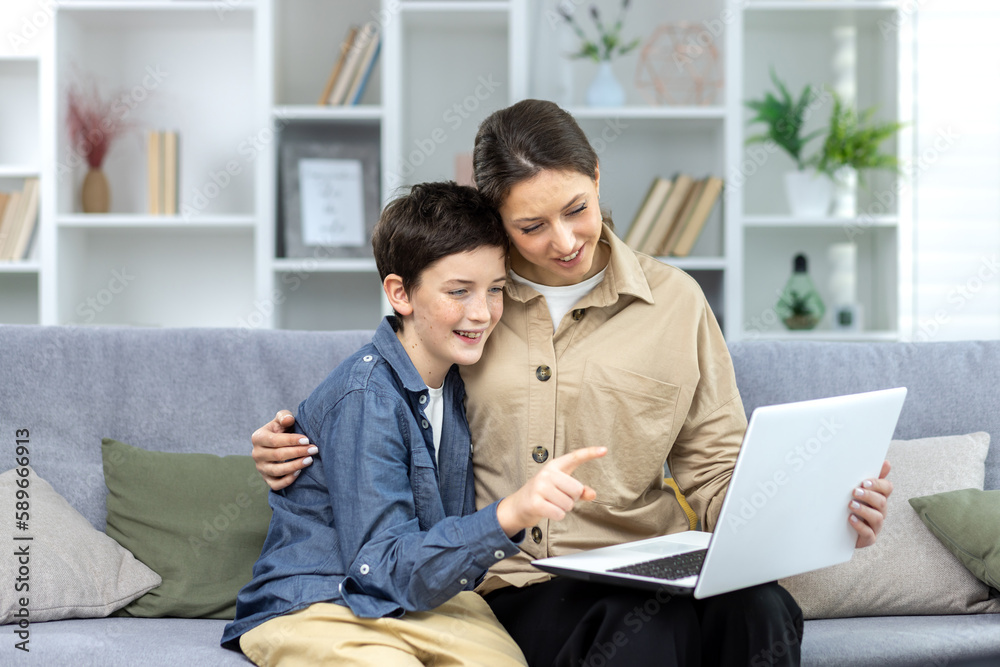 Portrait of family, mother and teenage son sitting on sofa at home, holding laptop. They talk on a video call, study, watch a movie, a photo together. Portrait of family, mother and teenage son sitting on sofa at home, holding laptop. They talk on a video call, study, watch a movie, a photo together.