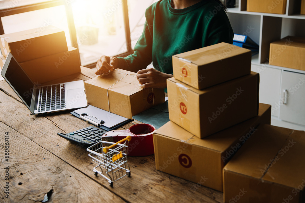 Fototapeta premium SME entrepreneur Small business entrepreneurs Online selling ideas,Happy Young Asian business owner work on computer and a boxs at home,delivery SME procurement package box deliver to customers,