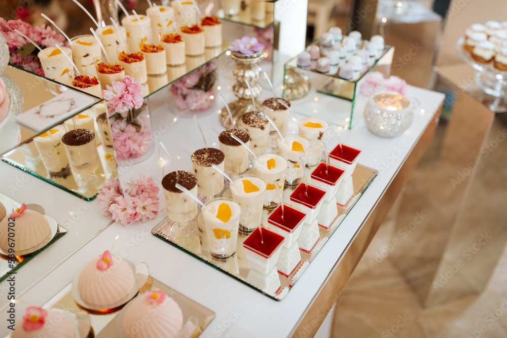 Delicious wedding reception candy bar dessert table full with cakes and sweets and flowers Chinese cherry blossoms on the background of an exquisite restaurant