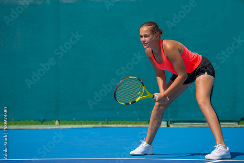 A girl plays tennis on a court with a hard blue surface on a summer sunny day © Павел Мещеряков