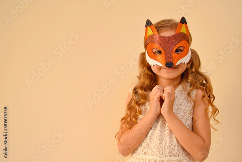 A child in a masquerade carnival mask of a fox, hand-made from glitter foamiran. Little cute cheerful comical girl in the role of a fox. The child is preparing for the carnival, holidays. photo