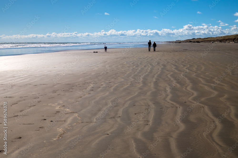 The almost deserted sandy beach at Foxton in New Zealand with several people silhouetted