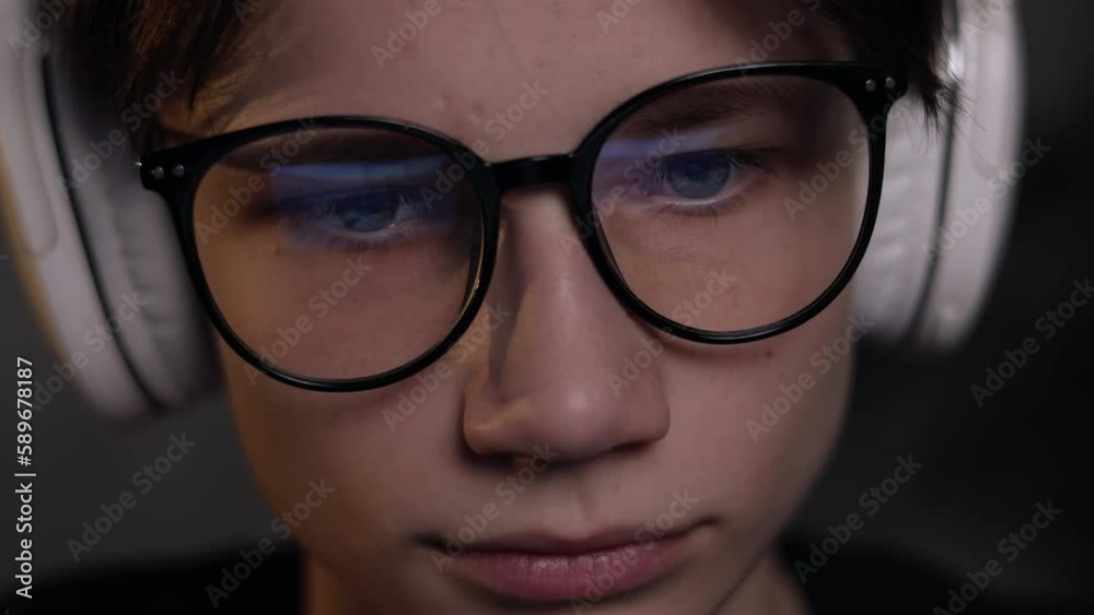 Young gamer man in glasses with screen reflection and headphones streaming live action game while explaining gameplay to subscribers. Gaming, esports, internet and virtual games at dark room. Young gamer man in glasses with screen reflection and headphones streaming live action game while explaining gameplay to subscribers. Gaming, esports, internet and virtual games at dark room.