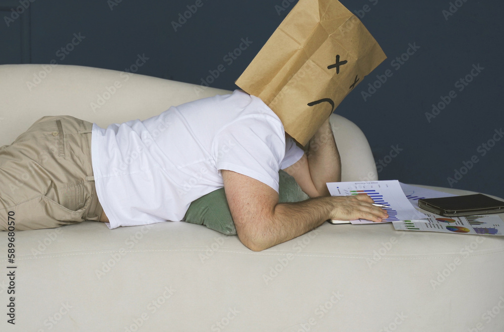 A man with a bag on his head with a drawn sad emoticon works with