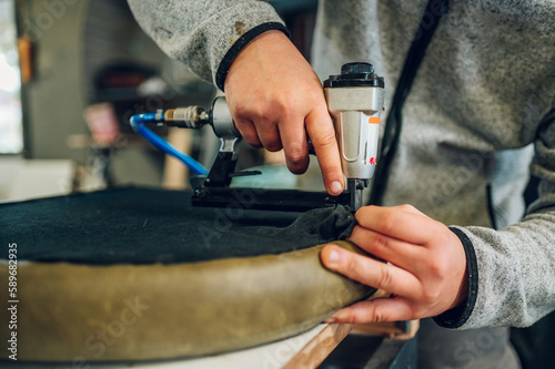 Fotografie Close up of a worker's hands upholstering a chair seat at the furniture workshop