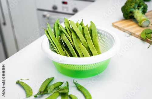 Green vegetables, romano helda beans, green peas and broccoli on the wooden cutting board. White kitchen table at home. The concept of a healthy nutrition and vegetarian lifestyle. Copy space photo