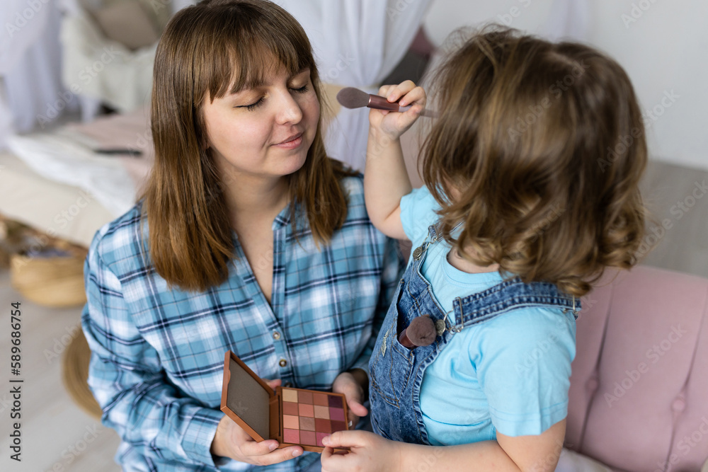 Pretty cute little girl doing make up for her mother with eye shadows palette, brush. Quality family time, enjoying domestic life, motherhood. Women's or Mother's Day celebration, having fun together Pretty cute little girl doing make up for her mother with eye shadows palette, brush. Quality family time, enjoying domestic life, motherhood. Women's or Mother's Day celebration, having fun together
