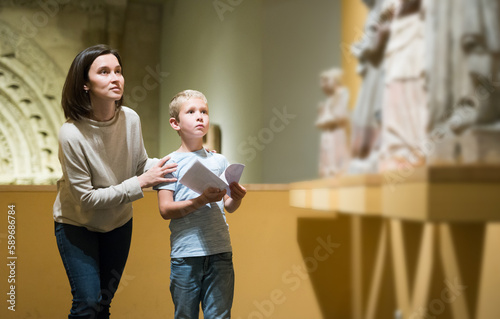 Young woman with son observing with interest sculptures exhibition in art museum